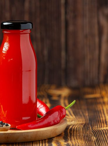 Chili sauce in bottle and peppers on dark wooden backgroud