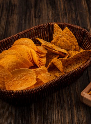 top-view-crispy-cone-shape-corn-snacks-wooden-divided-plate-with-shelled-sunflower-seeds-with-spicy-chips-bucket-with-popcorns-bowl-wooden-table-smoll